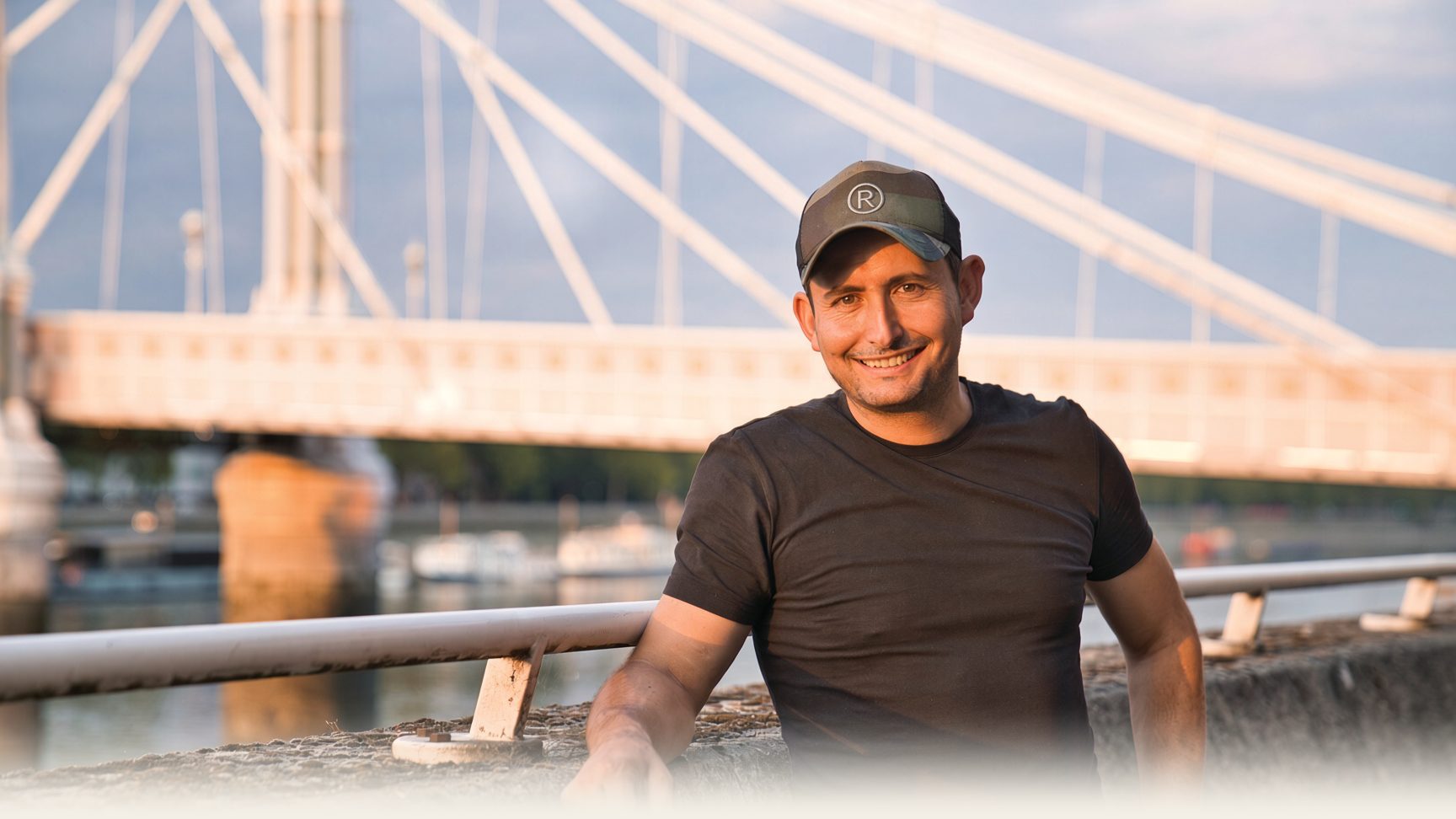 Roland Feizo smiling by the Albert Bridge in Chelsea, London.
