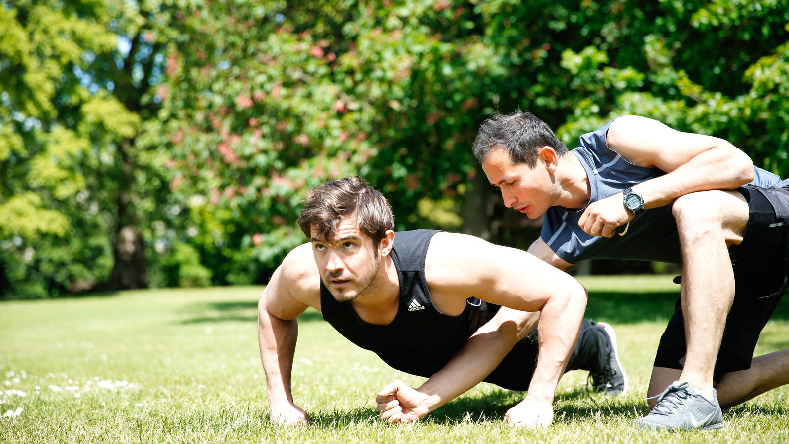 Roland coaching a client through a push-up on the grass in a park
